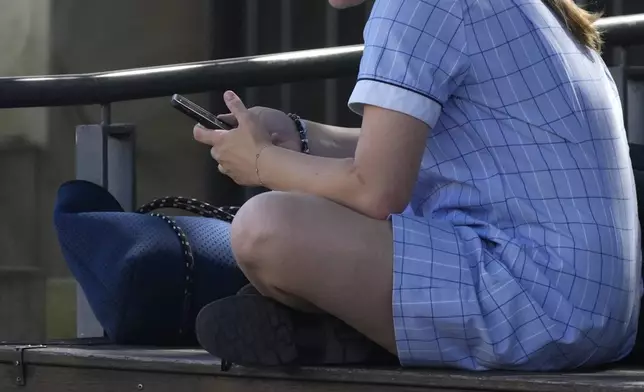 A young girl uses her phone while sitting on a bench in Sydney, Friday, Nov. 8, 2024. (AP Photo/Rick Rycroft)