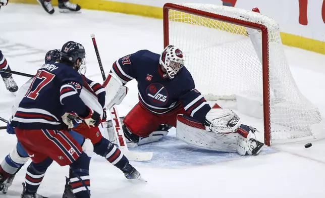 Winnipeg Jets goaltender Connor Hellebuyck (37) saves the shot from Colorado Avalanche's Calvin de Haan (44) as Adam Lowry (17) defends during the third period of an NHL hockey game Thursday, Nov. 7, 2024 in Winnipeg, Manitoba. (John Woods/The Canadian Press via AP)