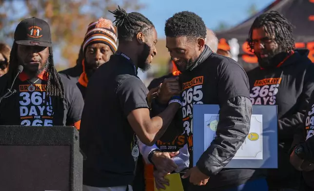 Baltimore Mayor Brandon Scott, right, embraces Adanus Sprillium during a press conference to celebrate achieving over 365 days without a homicide within the Brooklyn neighborhood Safe Streets catchment zone, Tuesday, Nov. 12, 2024, in Baltimore. (AP Photo/Stephanie Scarbrough)