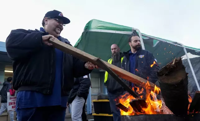 Boeing employee Adrian Camez, who works in Seattle, stokes the fire of a burn barrel as others arrive to vote on a new contract offer from the company Monday, Nov. 4, 2024, at the Aerospace Machinists Union hall in Renton, Wash. (AP Photo/Lindsey Wasson)