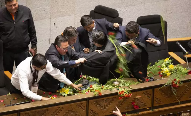 Security members shield Bolivian Vice President David Choquehuanca, third from left, from water and flowers thrown by lawmakers who support former President Evo Morales during the legislative session where the current president and vice president were to make a speech on the fifth anniversary of their government, in La Paz, Bolivia, Friday, Nov. 8, 2024. (AP Photo/Alejandro Mamani Apaza)