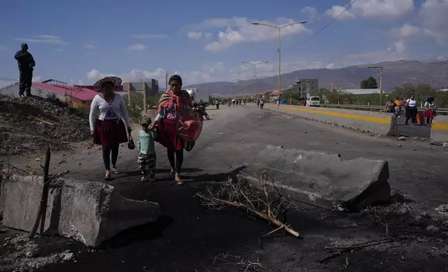 People walk on a road blocked by supporters of former President Evo Morales to prevent him from facing a criminal investigation over allegations of abuse of a minor and to demonstrate against an alleged assassination attempt, in Parotani, Bolivia, Thursday, Oct. 31, 2024. (AP Photo/Juan Karita)