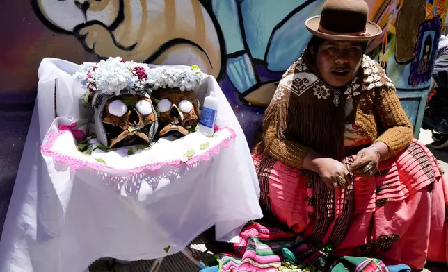 A woman sits next to her decorated human skulls at the General Cemetery as part of the annual “Ñatitas” festival, a tradition marking the end of the Catholic holiday of All Saints, in La Paz, Bolivia, Friday, Nov. 8, 2024. (AP Photo/Juan Karita)