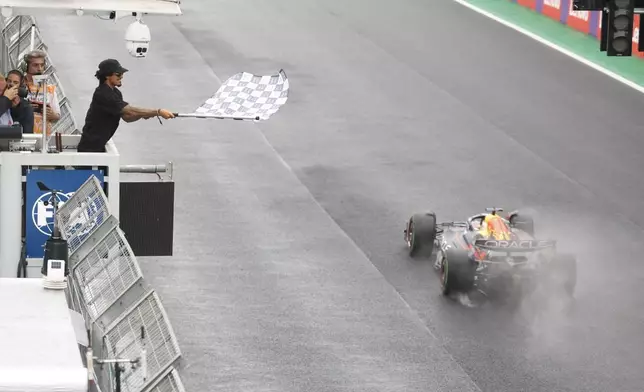 Red Bull driver Max Verstappen of the Netherlands takes the chequered flag waved by Brazilian surfer Gabriel Medina to win the Brazilian Formula One Grand Prix at the Interlagos race track in Sao Paulo, Brazil, Sunday, Nov.3, 2022. (Sebastian Moreira/Pool via AP)