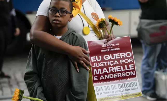 A demonstrator embraces a child while holding a sign with a message that reads in Portuguese: "I want justice for Marielle and Anderson", before the start of the trial of councilwoman Marielle Franco’s suspected murderers, outside the Court of Justice, in Rio de Janeiro, Brazil, Wednesday, Oct. 30, 2024. (AP Photo/Silvia Izquierdo)