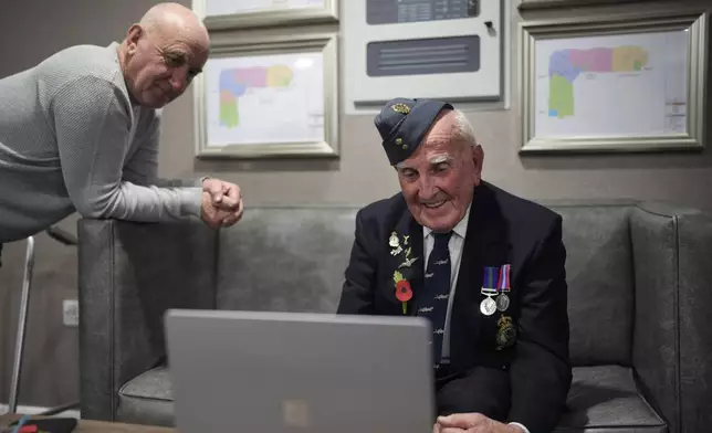 Michael Woods, 100-year-old World War II veteran, right, speaks during a video interview next to his son Eddie in Dunstable, Bedfordshire, England, Tuesday, Nov. 5, 2024. (AP Photo/Kin Cheung)