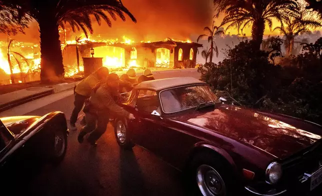 CORRECTS CAR - Firefighters and sheriff's deputies push a vintage car away from a burning home as the Mountain Fire burns in Camarillo, Calif., on Wednesday, Nov. 6, 2024. (AP Photo/Noah Berger)