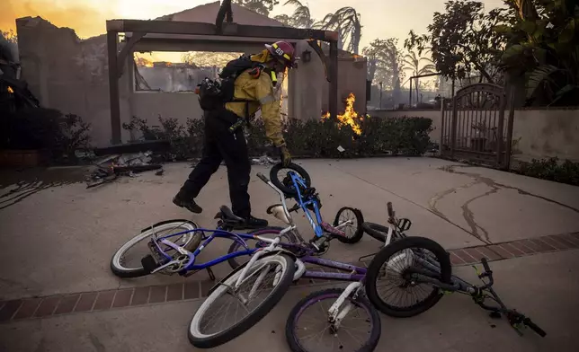 A firefighter, moves bicycles as he works against the Mountain fire, Wednesday, Nov. 6, 2024, near Camarillo, Calif. (AP Photo/Ethan Swope)