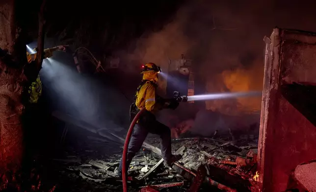 Firefighter Missy Forrett with the Beverly Hills Fire Department puts out flames at a home destroyed by the Mountain Fire in Camarillo, Calif., Wednesday, Nov. 6, 2024. (Stephen Lam/San Francisco Chronicle via AP)