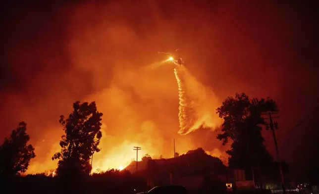 A helicopter drops water over flames in the Mountain fire, Wednesday, Nov. 6, 2024, near Santa Paula, Calif. (AP Photo/Ethan Swope)