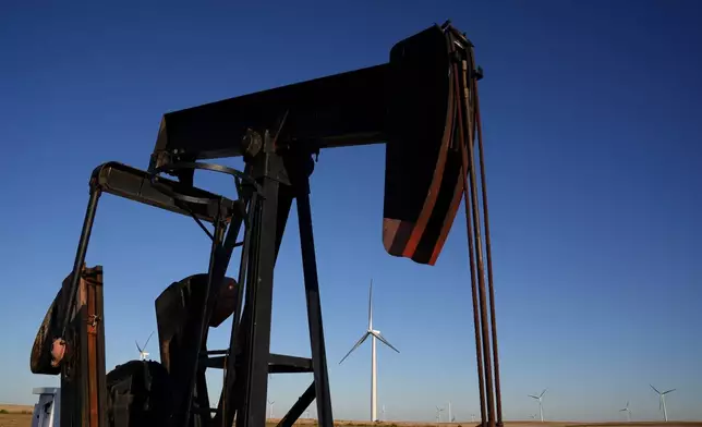 A pumpjack operates in the foreground as wind turbines at the Buckeye Wind Energy wind farm rise in the distance, Monday, Sept. 30, 2024, near Hays, Kan. (AP Photo/Charlie Riedel)