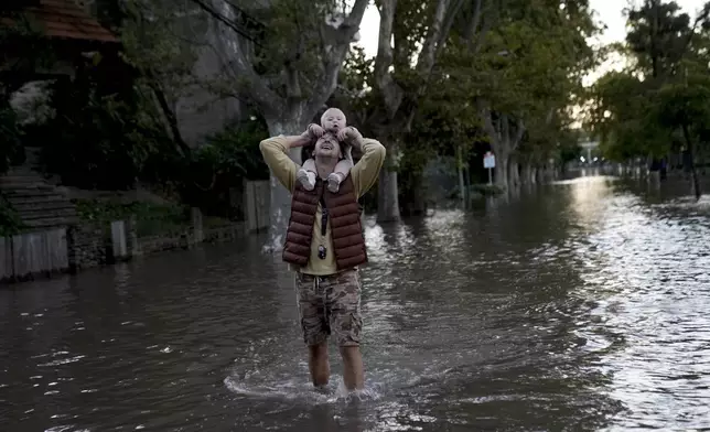 FILE - Alex Pusharev holds his daughter Miroslava while wading through a street flooded due to the rise of the water levels of the Rio de la Plata River, in Tigre, on the outskirts of Buenos Aires, Argentina, March 21, 2024. (AP Photo/Rodrigo Abd, File)