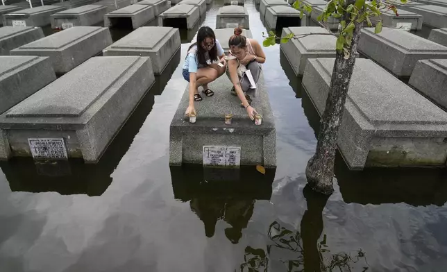 FILE - Women place candles on the half-submerged tomb of family members at flood-prone Holy Spirit Memorial Park in Masantol, Pampanga province, Philippines after heavy rains from recent tropical storm Trami caused water to become higher than usual, ahead of All Saints Day, Oct. 31, 2024. (AP Photo/Aaron Favila, File)