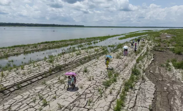 FILE - People walk through a part of the Amazon River that shows signs of drought in Santa Sofia, on the outskirts of Leticia, Colombia, Oct. 20, 2024. (AP Photo/Ivan Valencia, File)