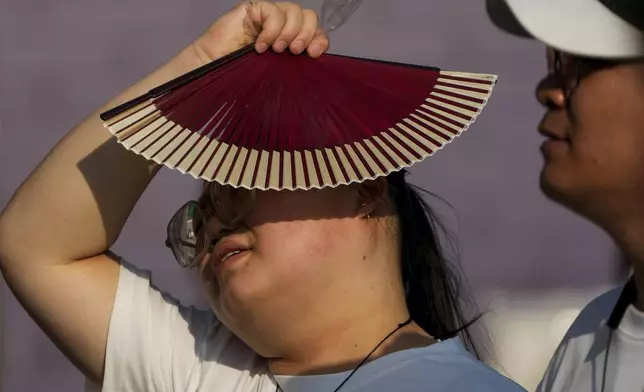 FILE - A woman uses a fan to block the sun as she walks with her companion on a hot day in Beijing, June 16, 2024. (AP Photo/Andy Wong, File)