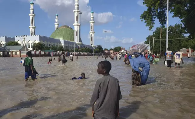 FILE - People walk through floodwaters following a dam collapse in Maiduguri, Nigeria, Tuesday, Sept 10, 2024. (AP Photos/ Joshua Olatunji, File)