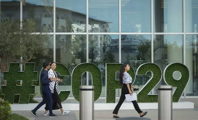 People walk by a sign for COP29, the United Nations Climate Change Conference, in Baku, Azerbaijan, Tuesday, Sept. 17, 2024. (AP Photo/Sergei Grits)