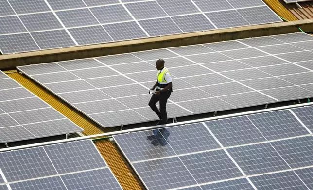 FILE - Mark Munyua, CP solar's technician, examines solar panels on the roof of a company in Nairobi, Kenya, Sept. 1, 2023. (AP Photo/Brian Inganga, File)