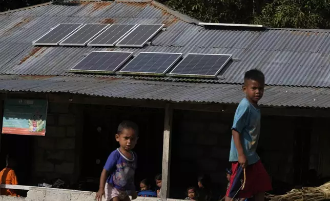 FILE - Children play near solar panels on the roof of house in Walatungga village on Sumba Island, Indonesia, March 21, 2023. (AP Photo/Dita Alangkara)