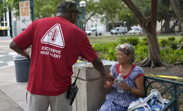 FILE - Ricky Leath, an outreach specialist with the City of Miami, talks with Bei Zhao, right, as he works with the Miami-Dade County Homeless Trust to distribute bottles of water and other supplies to the homeless population, helping them manage high temperatures, May 15, 2024, in Miami. (AP Photo/Lynne Sladky, File)