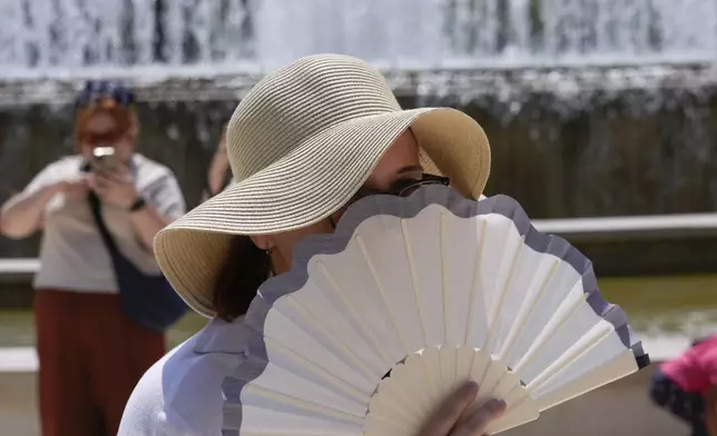 FILE - A tourist shelters from the sun by a fountain in front of the Sforzesco Castle in Milan, Italy, July 11, 2024. (AP Photo/Luca Bruno, File)