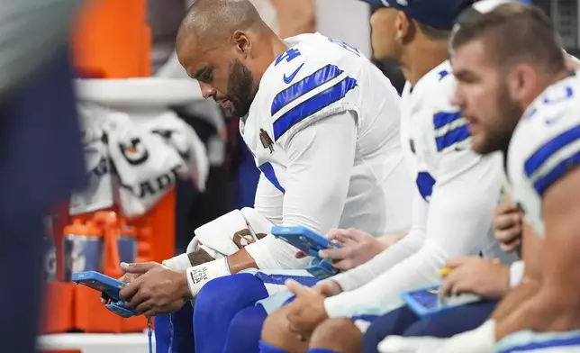 Dallas Cowboys quarterback Dak Prescott (4) reads a tablet on the bench during the first half of an NFL football game against the Atlanta Falcons, Sunday, Nov. 3, 2024, in Atlanta. (AP Photo/ Brynn Anderson)