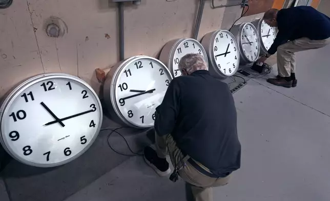 Clockmakers Rich Finn, left, and Tom Erb adjust the time zone controllers on a series of clocks that'll be installed at Paine Field in Everett, Wash., at the Electric Time Company, Wednesday, Oct. 30, 2024, in Medfield, Mass. (AP Photo/Charles Krupa)