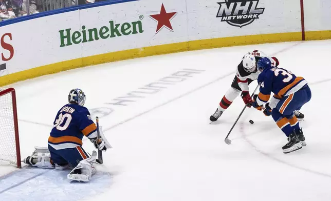 New York Islanders defenseman Grant Hutton (34) fights for the puck during the first period in an NHL hockey game against the New Jersey Devils Saturday, Nov. 9, 2024, in Elmont, N.Y. (AP Photo/Stefan Jeremiah)