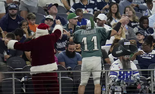 A fan dressed in a Santa Claus costume, celebrates with a Philadelphia Eagles fan as a Dallas Cowboys fan, sitting bottom right, and others watch play in the second half of an NFL football game in Arlington, Texas, Sunday, Nov. 10, 2024. (AP Photo/Julio Cortez)