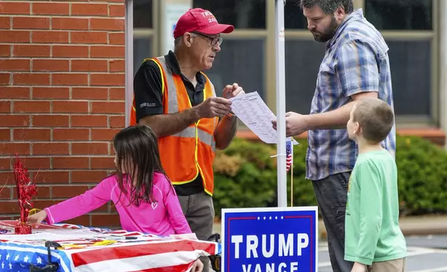 Glyn Hughes, left, gives Republican ballot information to Peter Dolan who came with his children, Zoe, left and P.J. to vote this morning at Reynolds Middle School on Election Day, Tuesday, Nov. 5, 2024 in Asheville, N.C. (AP Photo/Kathy Kmonicek)