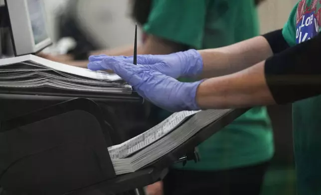 A county worker handles ballots in a scanning machine at a tabulating area at the Clark County Election Department, Saturday, Nov. 2, 2024, in North Las Vegas, Nev. (AP Photo/John Locher)