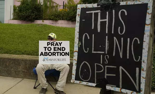 FILE - An anti-abortion supporter sits behind a sign that advises the Jackson Women's Health Organization clinic is still open in Jackson, Miss., Wednesday, July 6, 2022. (AP Photo/Rogelio V. Solis, File)