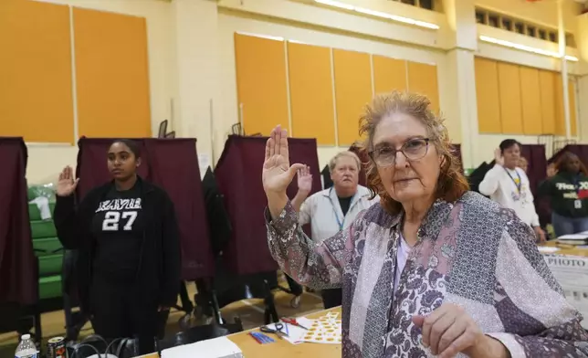 Holyn Robinson, a student at Xavier University, left, and Margie Robson, right, both first time precinct commissioners, take their oath along with fellow commissioners just before the opening of the polls, at the Hynes Charter School in New Orleans on Election Day, Tuesday, Nov. 5, 2024. (AP Photo/Gerald Herbert)