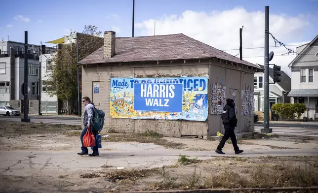 People pass a campaign sign on an abandoned building in Denver on Election Day, Tuesday, Nov. 5, 2024. (AP Photo/Chet Strange)