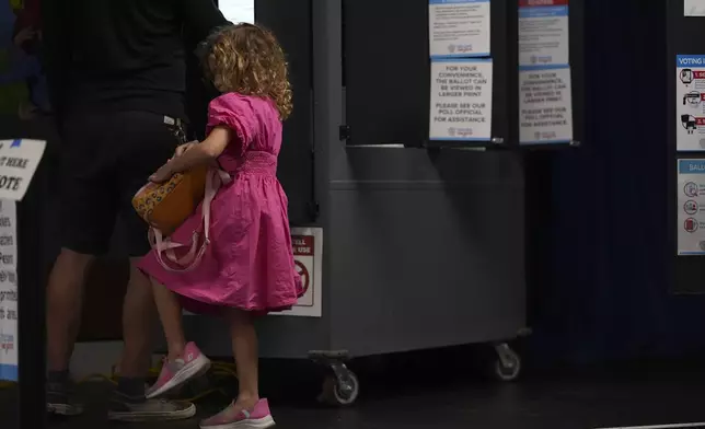 A young girl accompanies her father as he votes at a polling place inside Dad's Garage Theatre Company, Tuesday, Nov. 5, 2024, in Atlanta. (AP Photo/Brynn Anderson)