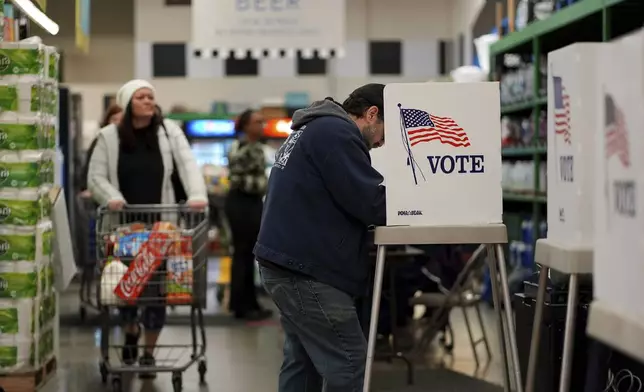 A woman shops while a voter casts a ballet at a grocery store, Tuesday, Nov. 5, 2024, in Lawrence, Kan. (AP Photo/Charlie Riedel)