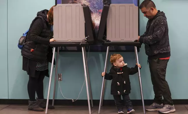 Oliver Barragan, 2, center, waits for his mother, Richelle Barragan, left, as she votes on Election Day at Werner Park, Tuesday, Nov. 5, 2024, in Papillion, Neb. (Liz Rymarev/Omaha World-Herald via AP)