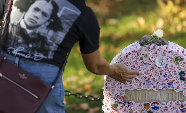 A voter wears a shirt with a picture of Kamala Harris as a young girl as they leave an "I voted" sticker on the headstone of Susan B. Anthony at Mount Hope Cemetery in Rochester, New York on Election Day, Tuesday, Nov. 5, 2024. (AP Photo/Lauren Petracca)