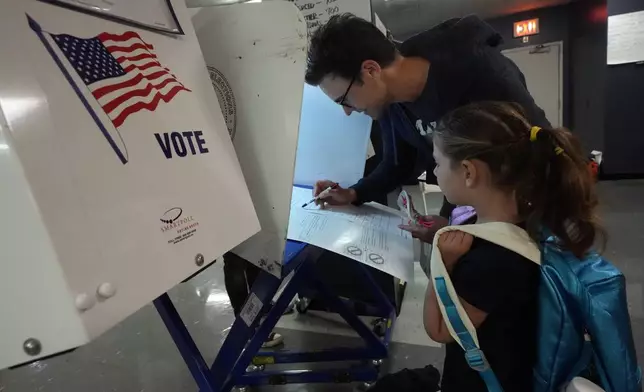 Benay Gould, 7, watches as her dad Charles Herschel marks his ballot at P.S. M811, The Mickey Mantle School, in New York, Tuesday, Nov. 5, 2024. (AP Photo/Richard Drew)