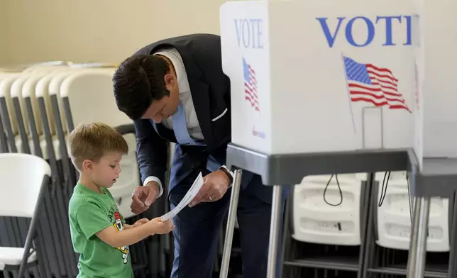 Zeb Smathers, shows a ballot to his 4-year-old son, Stone Smathers, while voting, Tuesday, Nov. 5, 2024, in Canton, N.C. (AP Photo/George Walker IV)