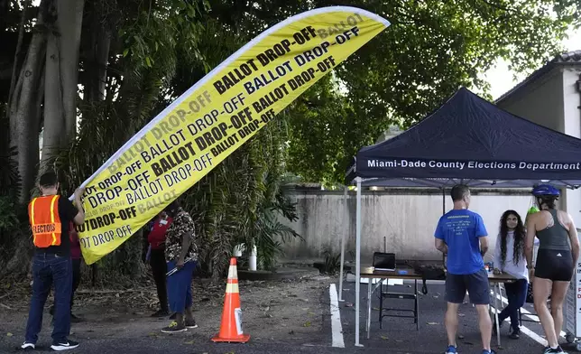 A poll worker puts up a sign for a ballot drop off location on the first day of early voting in the general election Monday, Oct. 21, 2024, in Miami. (AP Photo/Lynne Sladky)