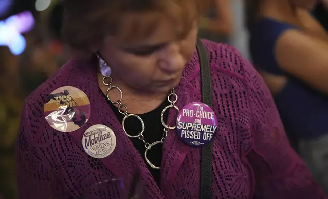 Denise Yettow wears a pair of buttons she saved from the 1989 Mobilize for Women's Lives Rally, as she gathers with supporters of Florida's Amendment 4, which would enshrine abortion rights in the state, for a watch party for the Yes On 4 campaign, on Election Day, Tuesday, Nov. 5, 2024, in St. Petersburg, Fla. (AP Photo/Rebecca Blackwell)