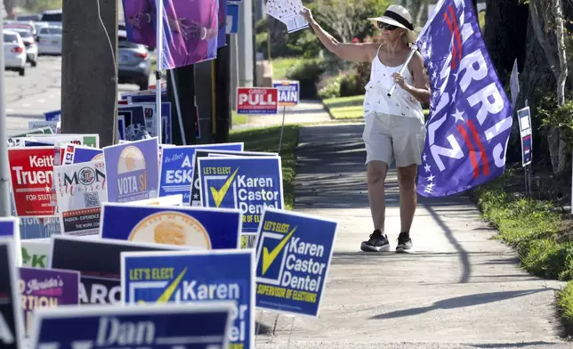 A campaign volunteer carries a Harris-Walz flag while waving to voters in line during early voting at the Orange County Supervisor of Elections precinct on Kaley Avenue in Orlando, Fla., Friday, Oct. 25, 2024. (Joe Burbank/Orlando Sentinel via AP)