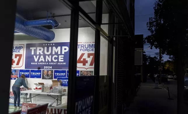 Volunteer Kim Tocco, left, positions yard signs in a campaign office for Republican presidential nominee former President Donald Trump, the night before the general election Monday, Nov. 4, 2024, in Hamtramck, Mich. (AP Photo/David Goldman)