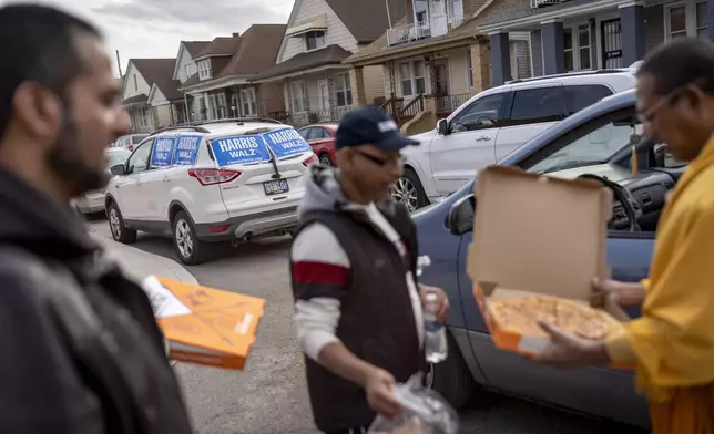 Posters for Democratic presidential nominee Vice President Kamala Harris are seen outside a polling site as Dharmananda Mahaprabu Barua, right, a Buddhist monk and supporter of Republican presidential nominee former President Donald Trump, brings pizza to fellow Trump supporters campaigning, Tuesday, Nov. 5, 2024, in Hamtramck, Mich. (AP Photo/David Goldman)