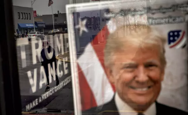 An image of Republican presidential nominee former President Donald Trump hangs in the window of a campaign office as a pedestrian passes by Monday, Nov. 4, 2024, in Hamtramck, Mich. (AP Photo/David Goldman)