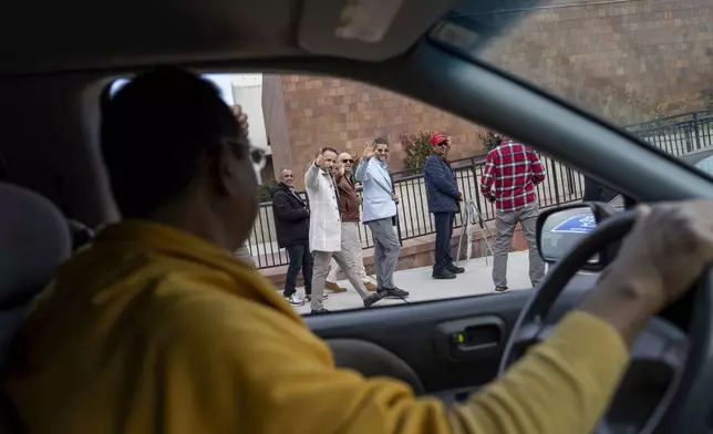 Dharmananda Mahaprabu Barua, a Buddhist monk and supporter of Republican presidential nominee former President Donald Trump, waves to Amer Ghalib, third from right, Hamtramck's Democratic Muslim mayor and fellow Trump supporter, as he drives through Hamtramck, Mich., on Election Day, Tuesday, Nov. 5, 2024. (AP Photo/David Goldman)