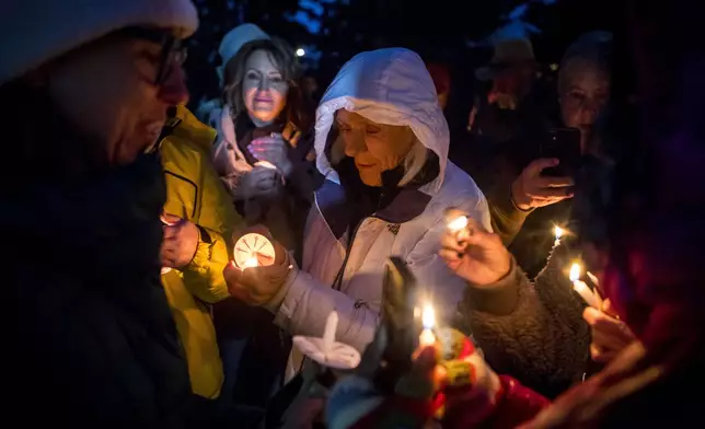 Rosalis Estes, center, keeps her candle lit in the drizzle at a vigil for grizzly bear No. 399 in Jackson, Wyo., Saturday Nov. 2, 2024. (AP Photo/Amber Baesler)