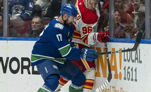 Vancouver Canucks' Filip Hronek, left, and Calgary Flames' Andrei Kuzmenko battle along the boards during first period NHL hockey action in Vancouver, B.C., Tuesday, November 12, 2024. (Rich Lam/The Canadian Press via AP)