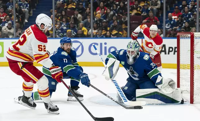 Vancouver Canucks goalie Kevin Lankinen (right) squares up to stop Calgary Flames' MacKenzie Weegar (left) as Canucks' Filip Hronek defends during first period NHL hockey action in Vancouver, B.C., Tuesday, November 12, 2024. (Rich Lam/The Canadian Press via AP)